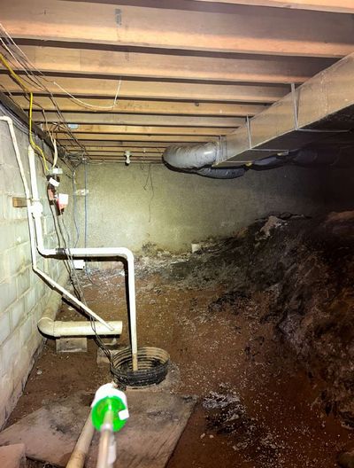 Crawl space beneath commercial building in Perkasie PA showing mold-covered floor, sump area, and evidence of chronic moisture and flooding