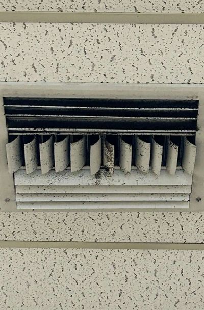 Close-up angle showing mold buildup along the vanes and housing of a contaminated HVAC supply register in a commercial office suite in Aston, PA