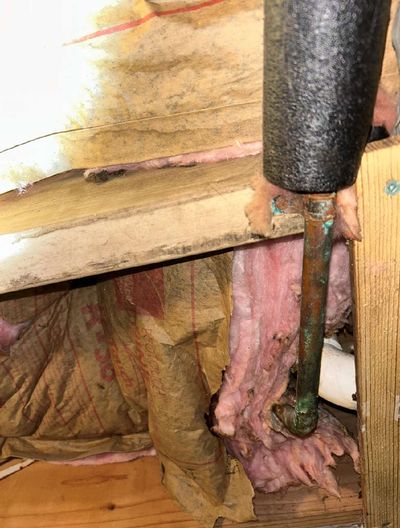 Water-damaged basement ceiling insulation pulled away from joists with a corroded copper pipe visible — slow leak feeding mold growth in Germantown Philadelphia