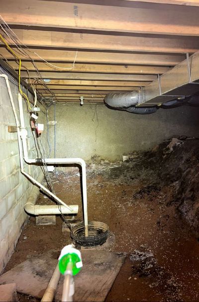 Wet crawl space with a muddy dirt floor, standing moisture, and a sump pit beneath a Dublin PA commercial building, identified as the moisture source during June 2026 mold testing