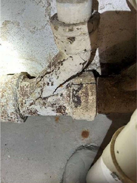Cracked cast iron waste drain pipe in a Roxborough, PA basement documented during a home inspection, showing corrosion along the aged drain line