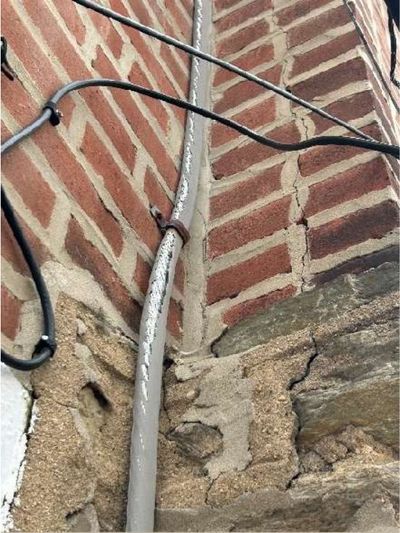 Frayed service entrance cable with cracked outer insulation running down brick at 7015 Large St Northeast Philadelphia, photographed during a May 2026 home inspection