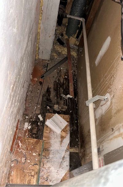Opened wall and floor cavity revealing dark, water-damaged framing and subfloor in a Philadelphia rowhome utility area