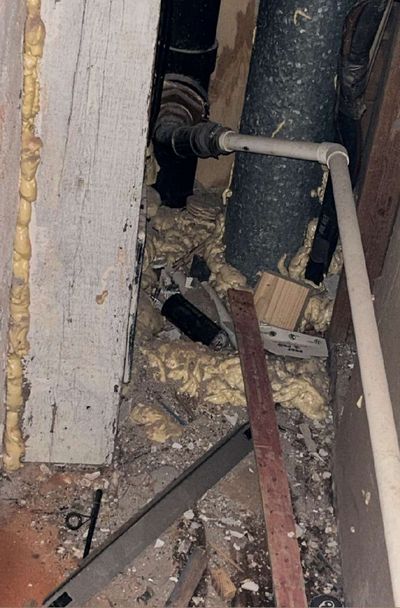 Insulation, piping, and stained framing inside the HVAC closet wall void of a Philadelphia rowhome, showing signs of ongoing moisture