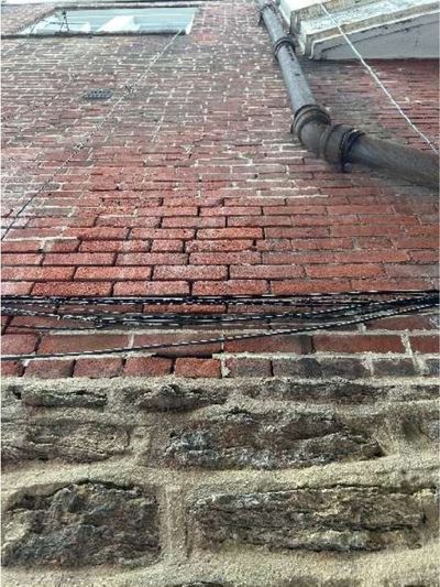 Open and deteriorated brick mortar joints on the rear masonry wall of a Fern Rock Philadelphia rowhome, with loose wiring, documented during a home inspection