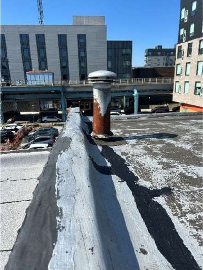 Worn flat roof with standing water and a corroded vent stack on a century-old Lawncrest row home in Northeast Philadelphia, documented during a home inspection